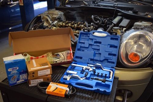 A box of tools is sitting on a table next to a mini cooper with the hood open.