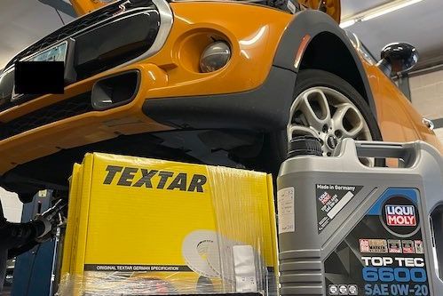 A mini cooper is sitting on a lift next to a bottle of liqui moly oil.