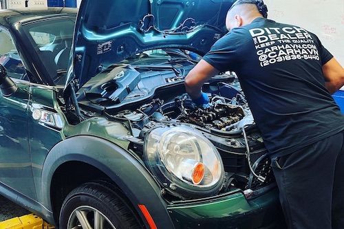 A man is working on the engine of a green mini cooper.