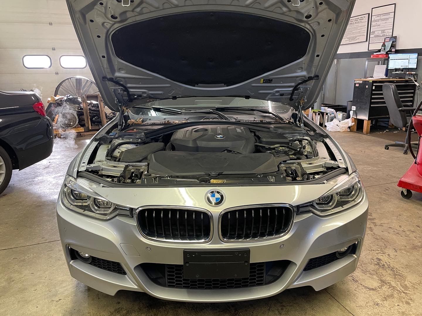 The hood of a silver bmw is open in a garage.