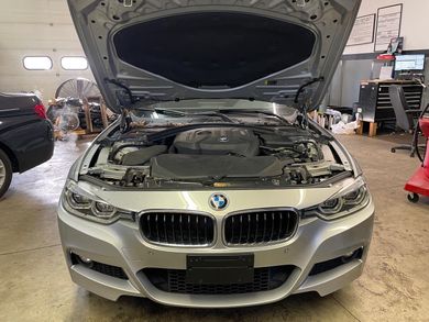 The hood of a silver bmw is open in a garage.