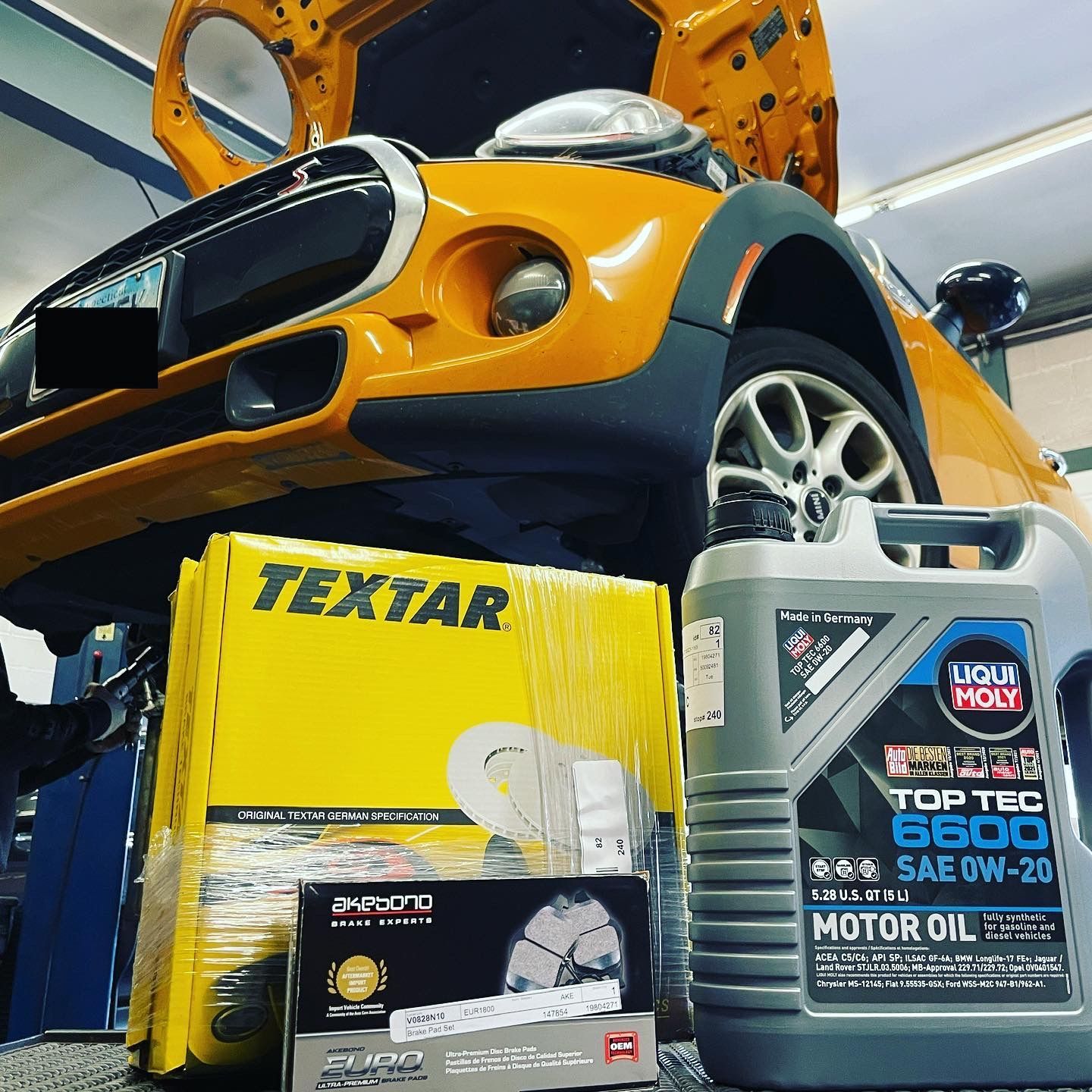A car with the hood up and a bottle of textar motor oil
