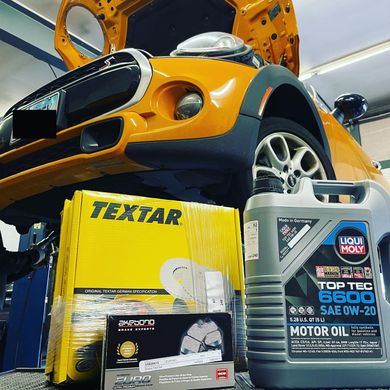 A car with the hood up and a bottle of textar motor oil