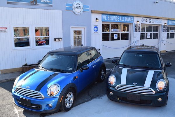 Two blue and black mini cooper cars are parked in front of a car dealership.