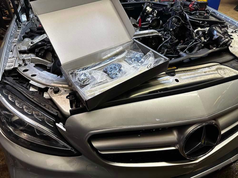 A silver mercedes with the hood open and a box of tools on the hood.