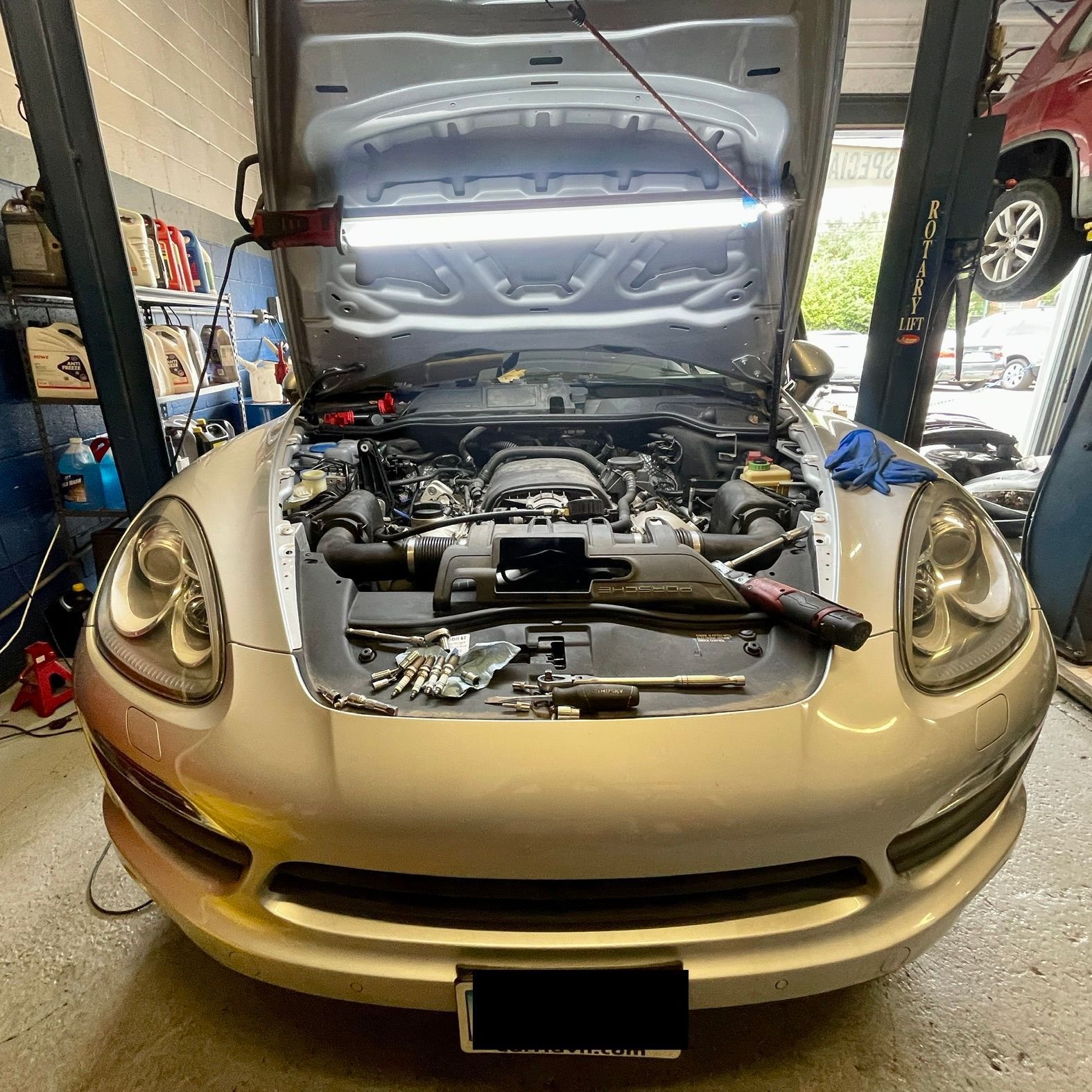 A car is being worked on in a garage with the hood open.