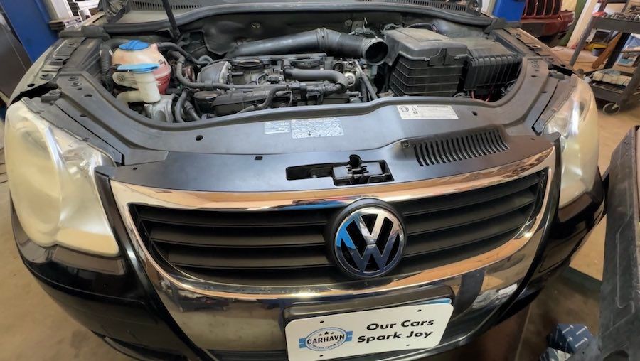 A black volkswagen with the hood up in a garage.