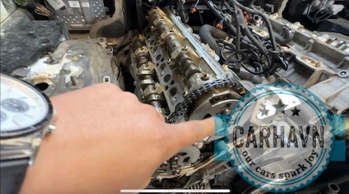 A person is working on a car engine with a watch on their wrist.