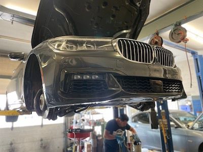 A man is working on a bmw on a lift in a garage.