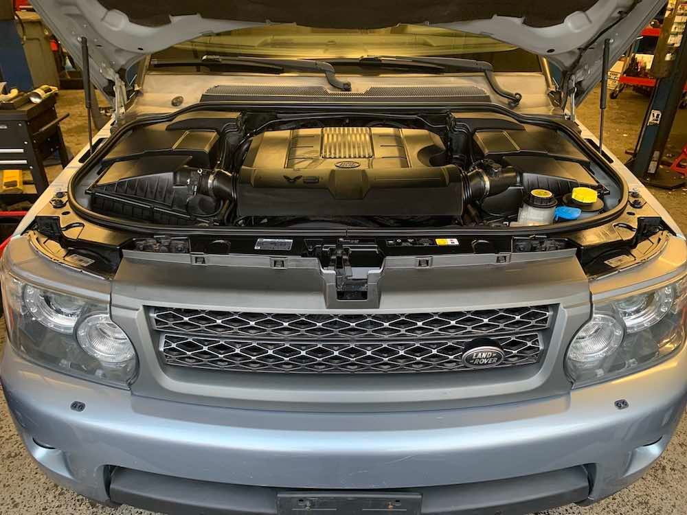The engine of a silver range rover sport is shown with the hood open.
