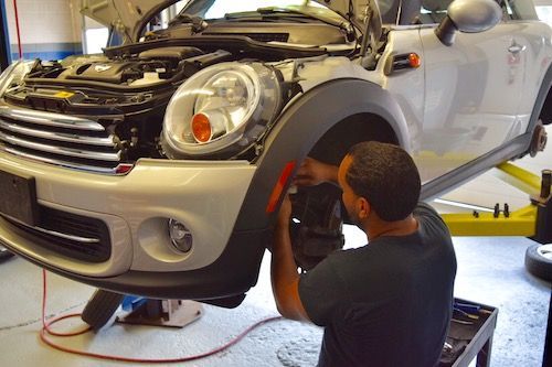 A man is working on a white mini cooper at CarHavn