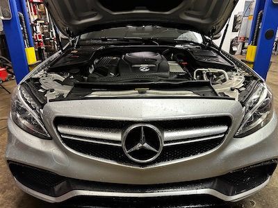 The hood of a mercedes benz is open in a garage.