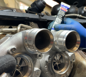 A person is holding a tube of lubricant on top of a turbocharger