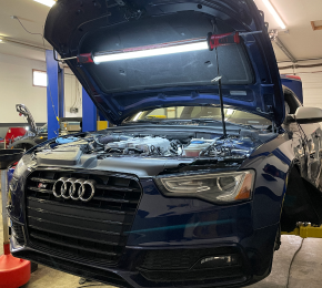 A blue audi with the hood open in a garage