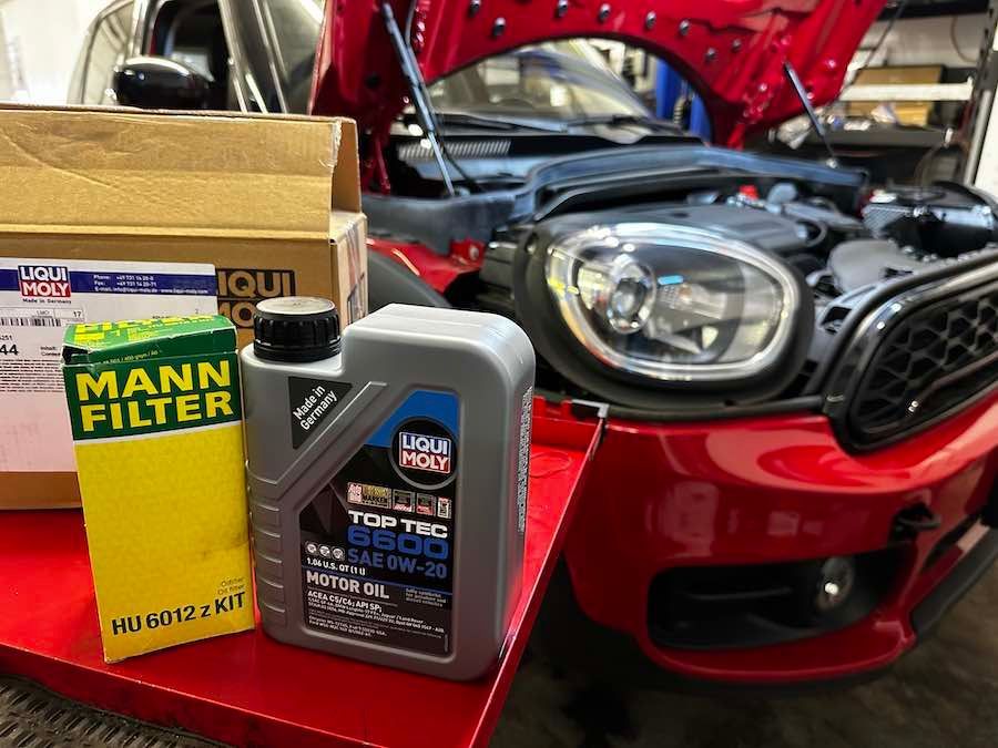 A red car with the hood open is sitting on a red table next to a bottle of oil.