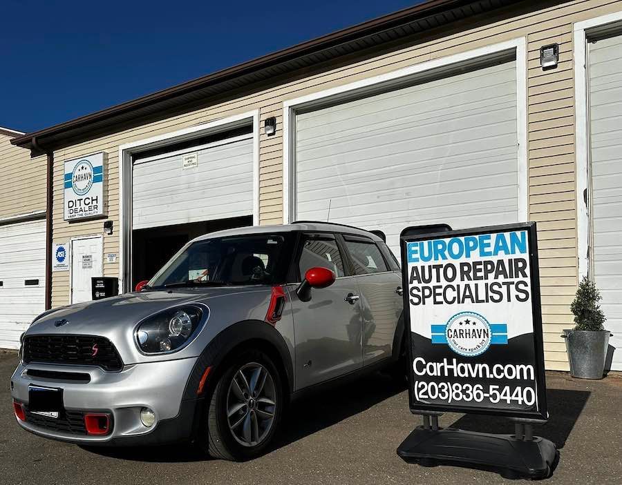 A silver mini cooper is parked in front of a car repair shop.