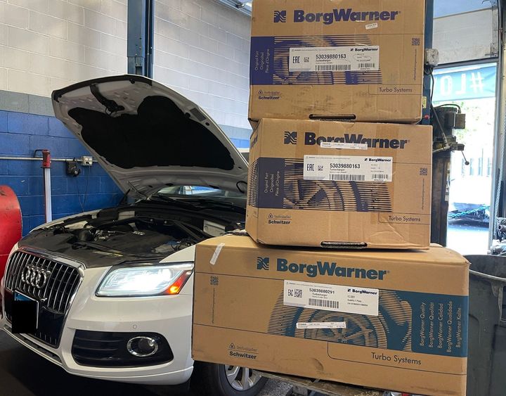 A car with the hood open is sitting in a garage next to boxes that say borgwarner