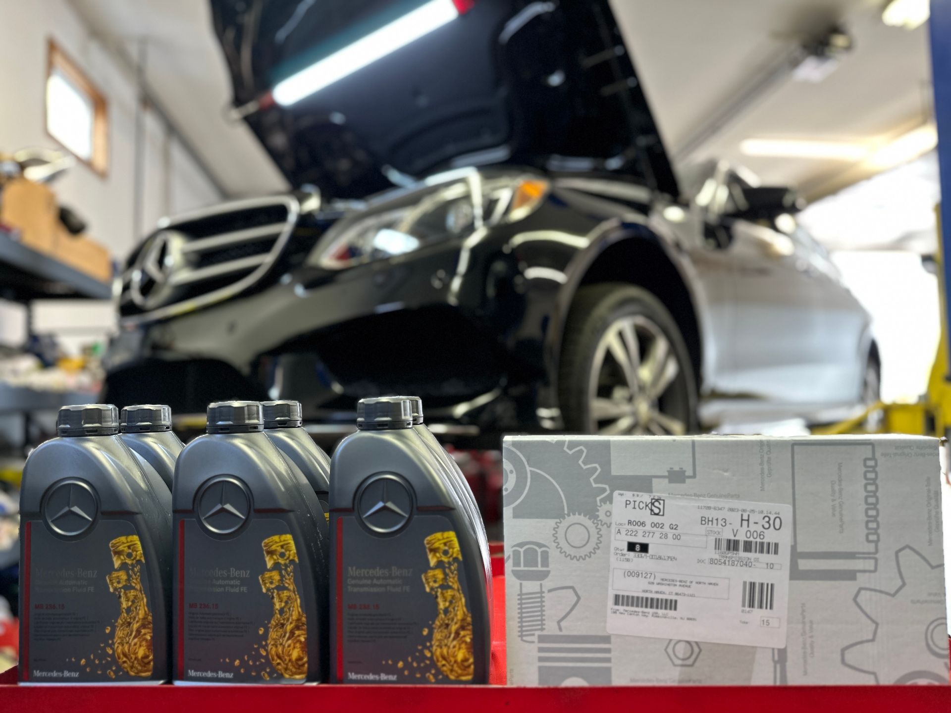 A mercedes is sitting on a lift in a garage next to bottles of oil