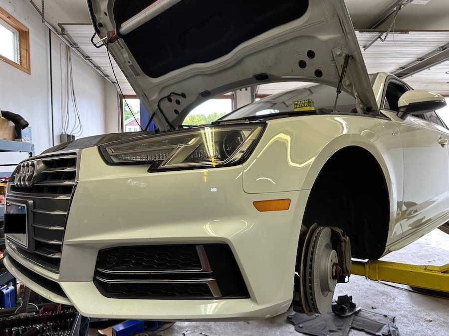 A white car with the hood open is sitting on a lift in a garage.