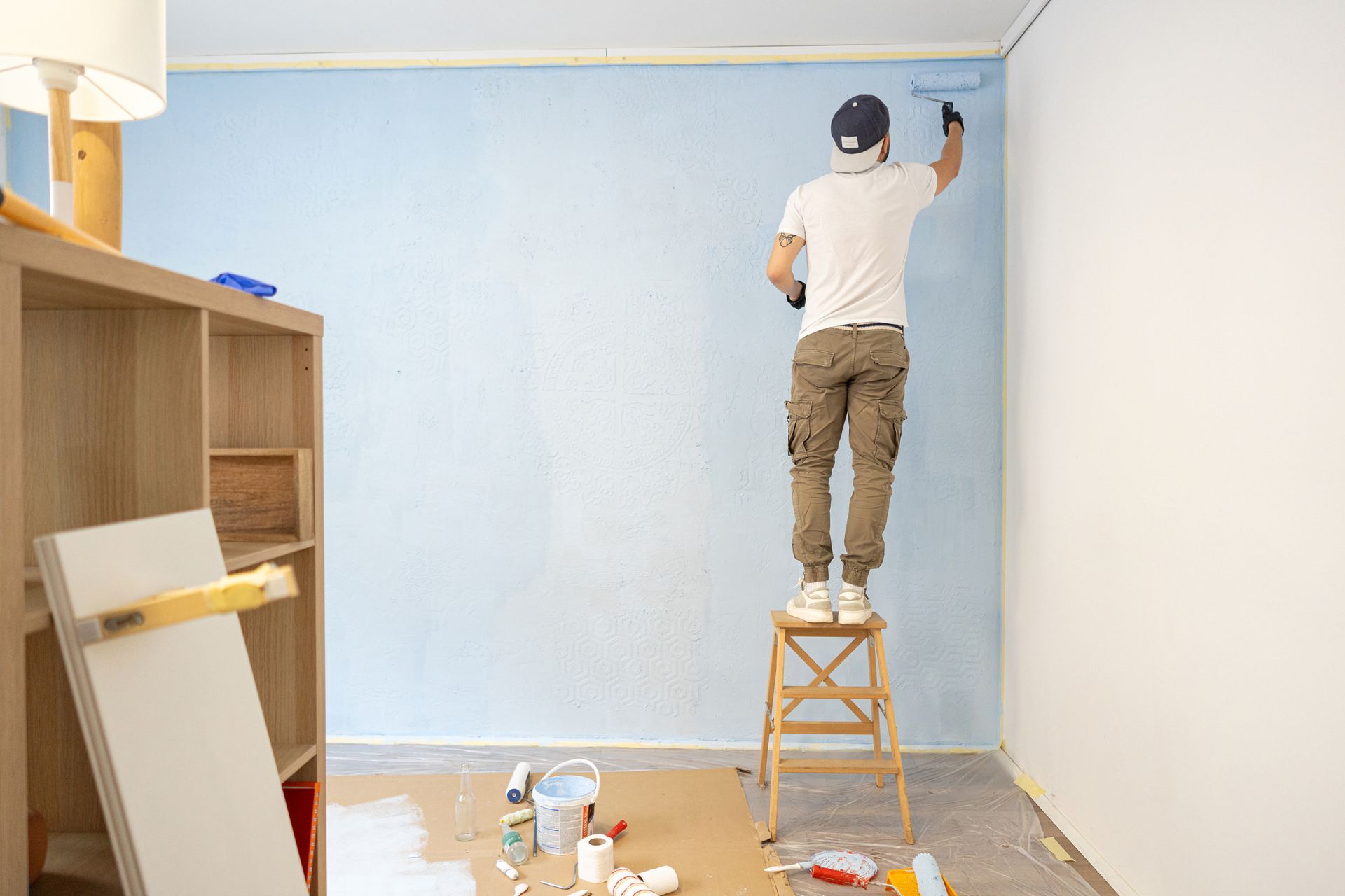 A man is standing on a ladder painting a wall.