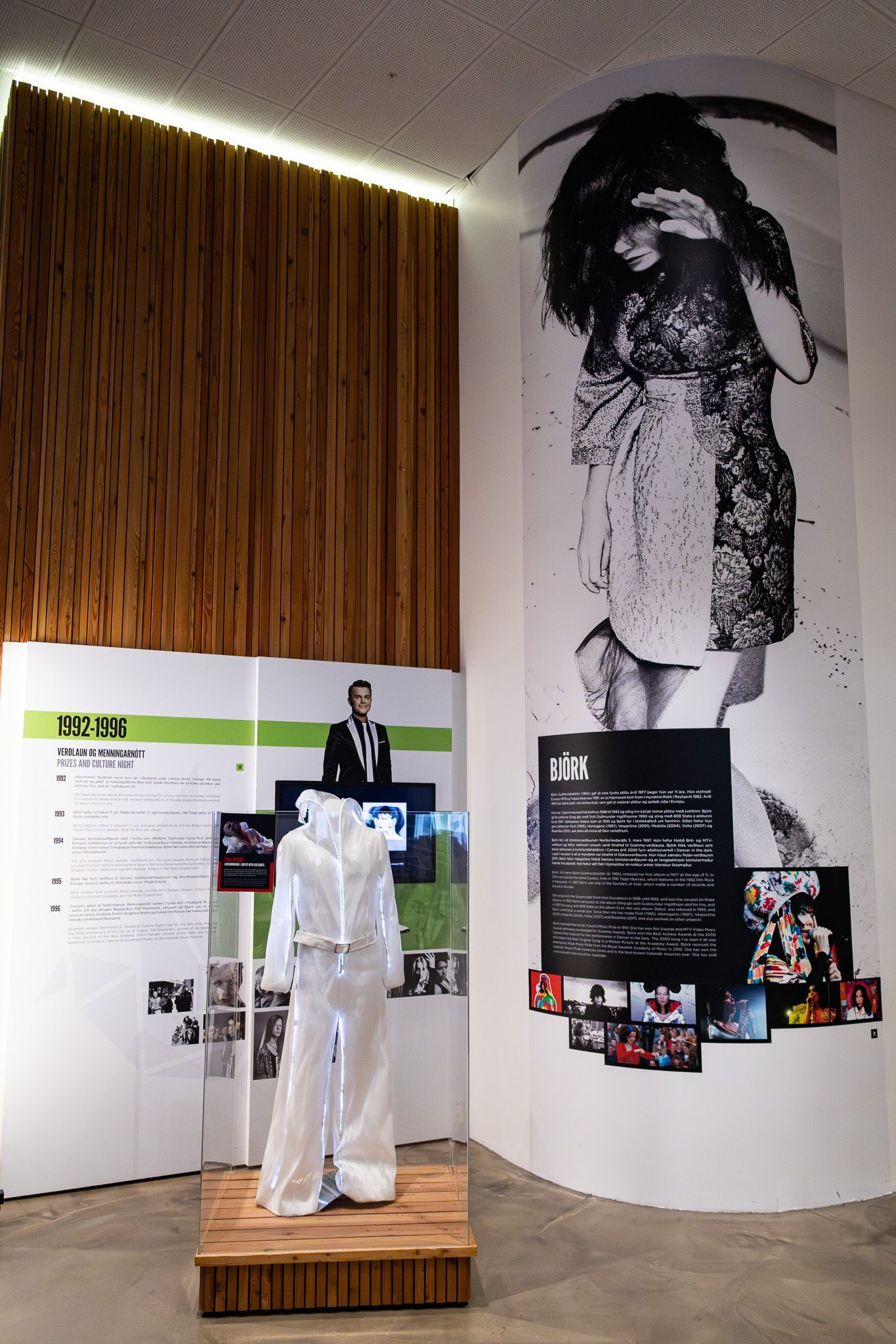Björk exhibition wall featuring a large portrait, timeline display, and iconic white stage outfit.
