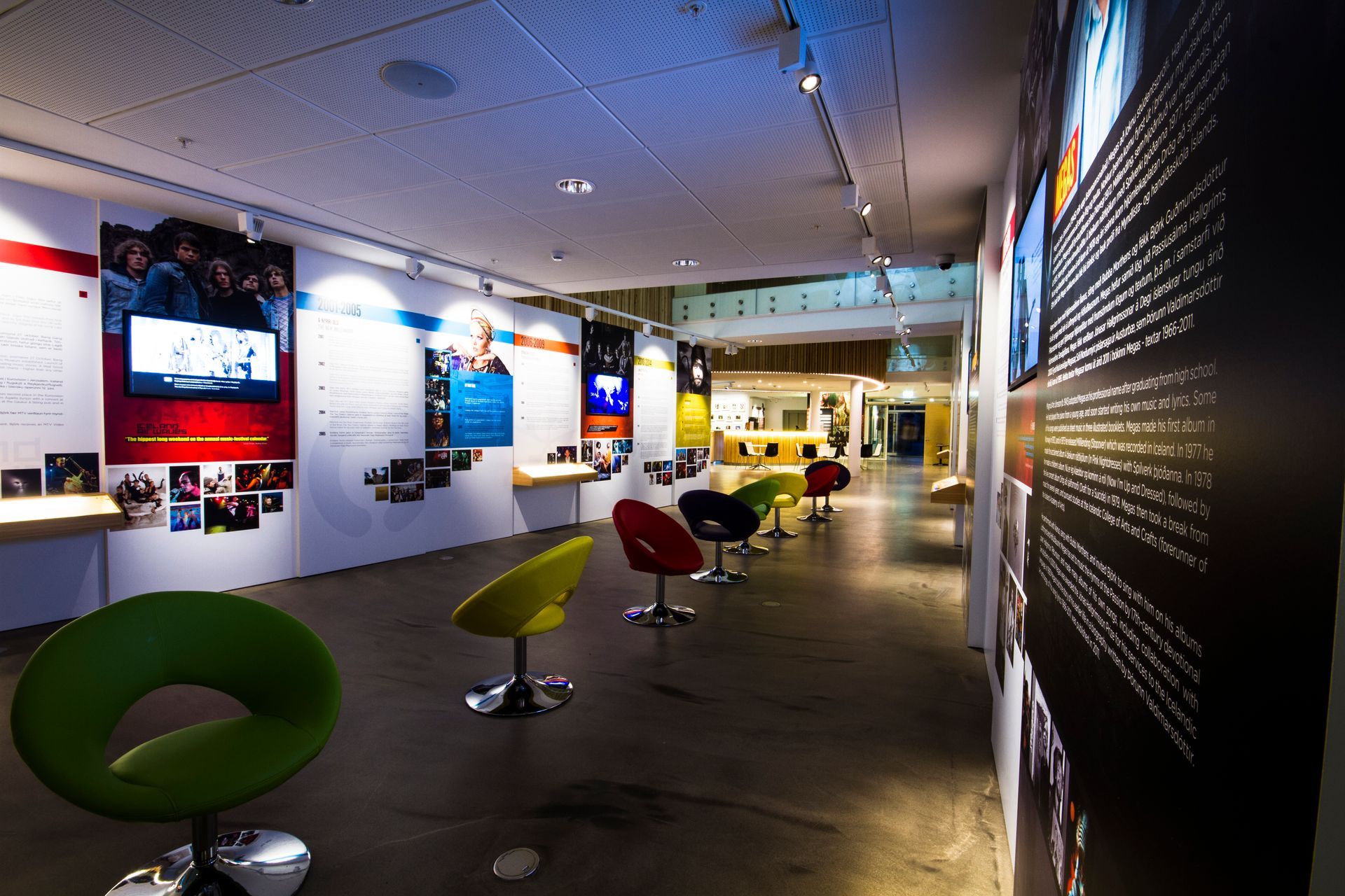 Exhibition hall at the Icelandic Museum of Rock ’n’ Roll with displays, screens, and colorful chairs.