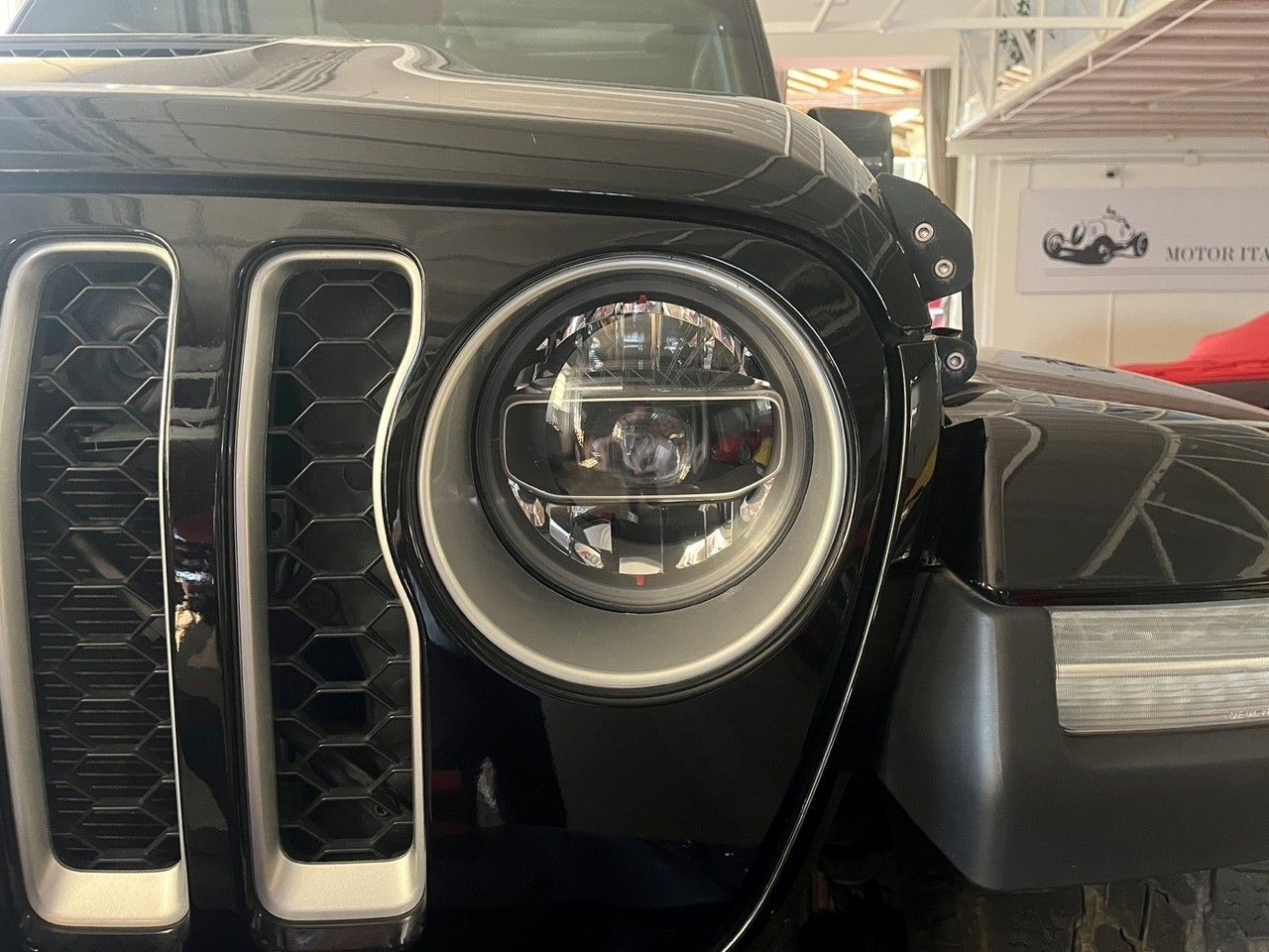 Primo piano della griglia nera e del faro rotondo di una Jeep in uno showroom.