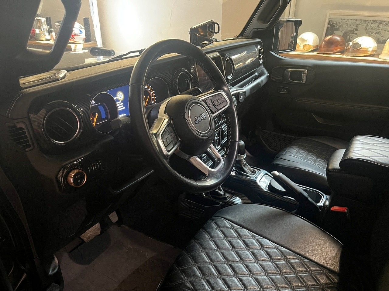 Interno di una Jeep nera con sedili trapuntati, volante e cruscotto illuminati di blu.