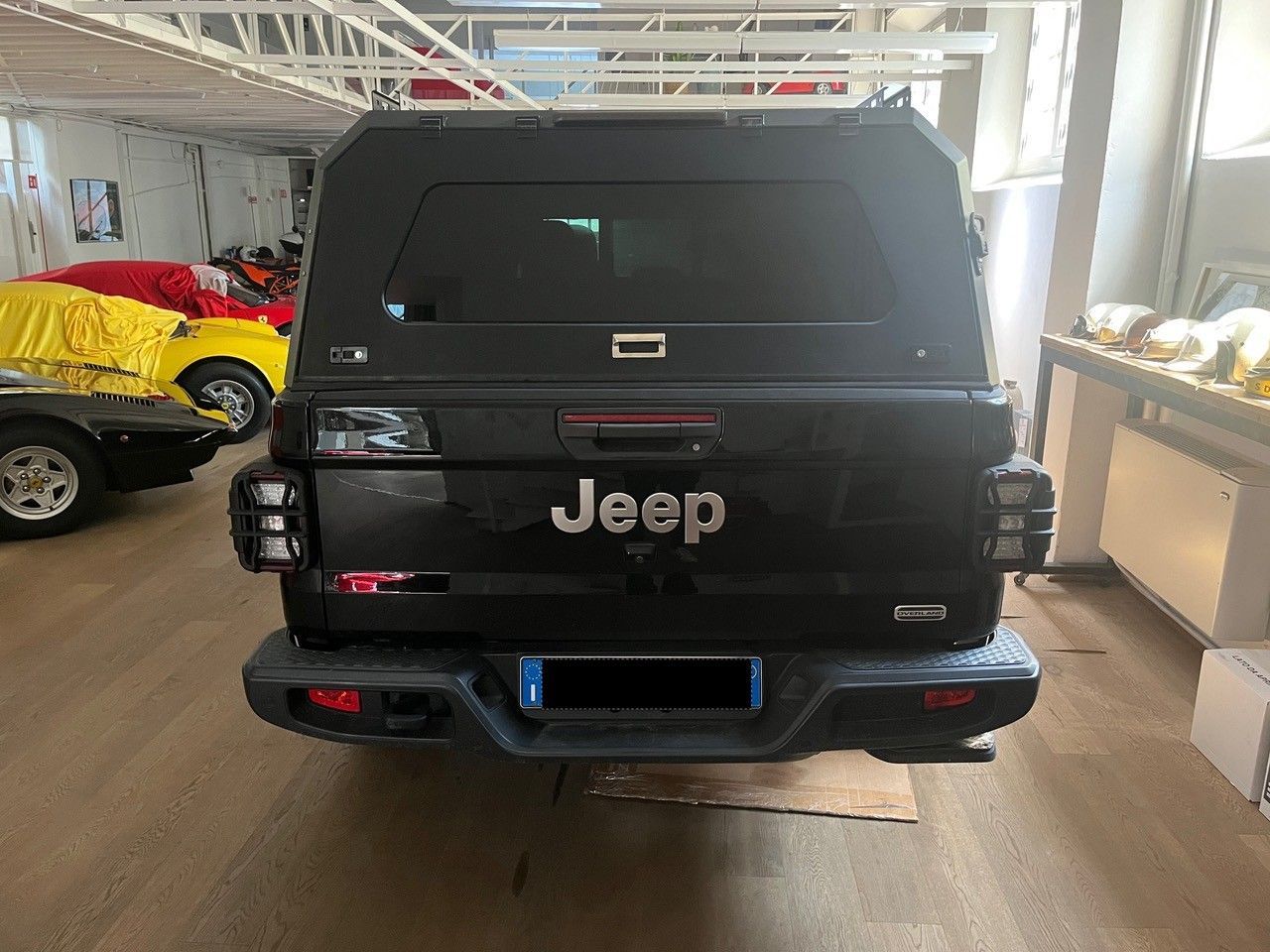 Jeep SUV nera vista da dietro in uno showroom, con un'auto gialla sullo sfondo.