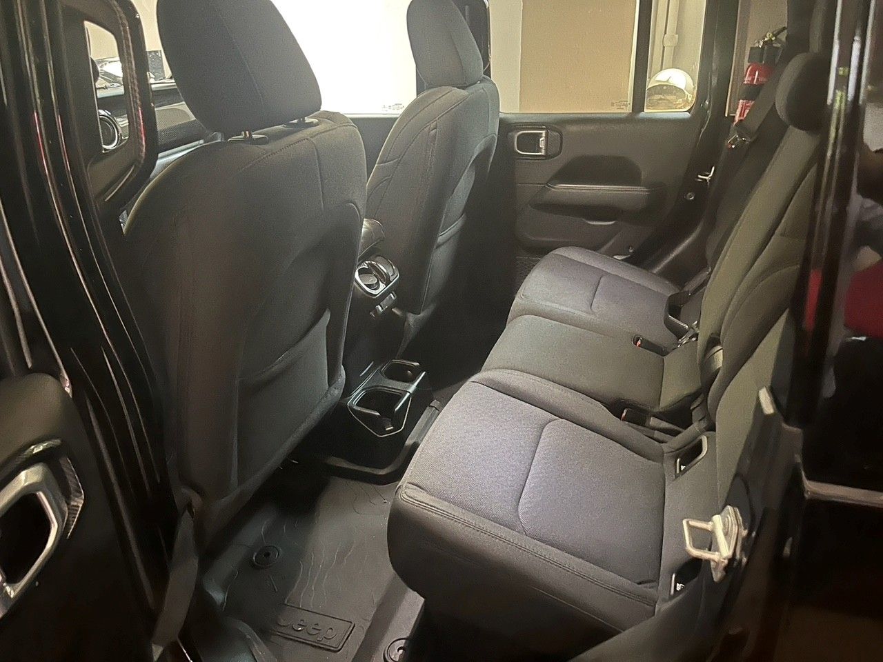 Interno dell'auto con due file di sedili in tessuto nero e console centrale, visto dalla portiera posteriore.