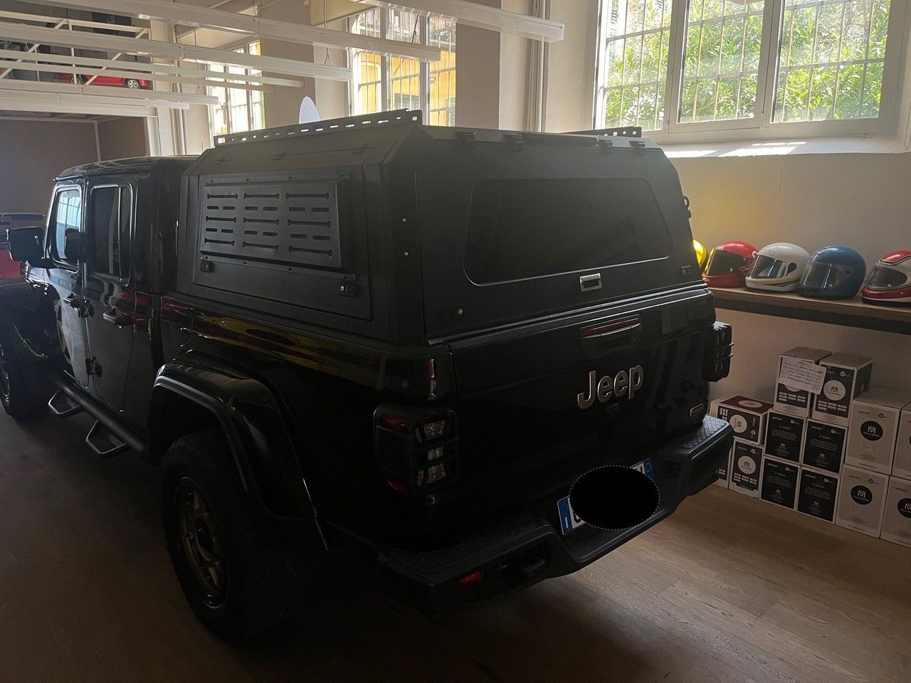 Un SUV Jeep nero è parcheggiato all'interno, accanto a scaffali e scatole, vicino a una finestra luminosa.
