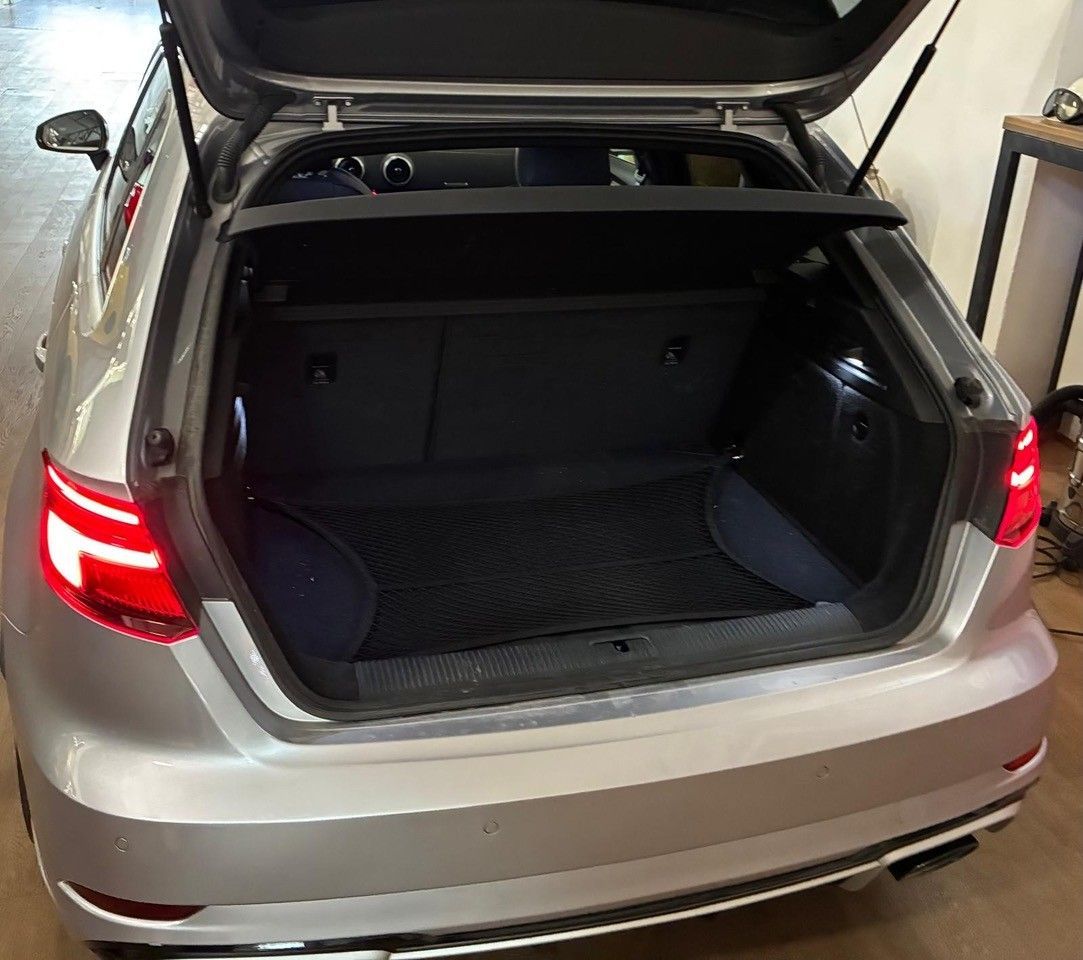 Bagagliaio aperto di una berlina argentata in un garage, che mostra il vano di carico vuoto.