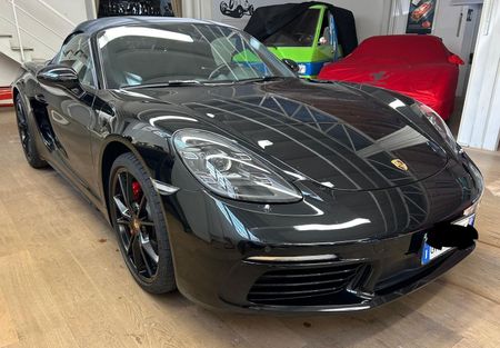 Una raffinata Porsche decappottabile nera parcheggiata all'interno di uno showroom, con altri veicoli coperti visibili sullo sfondo.