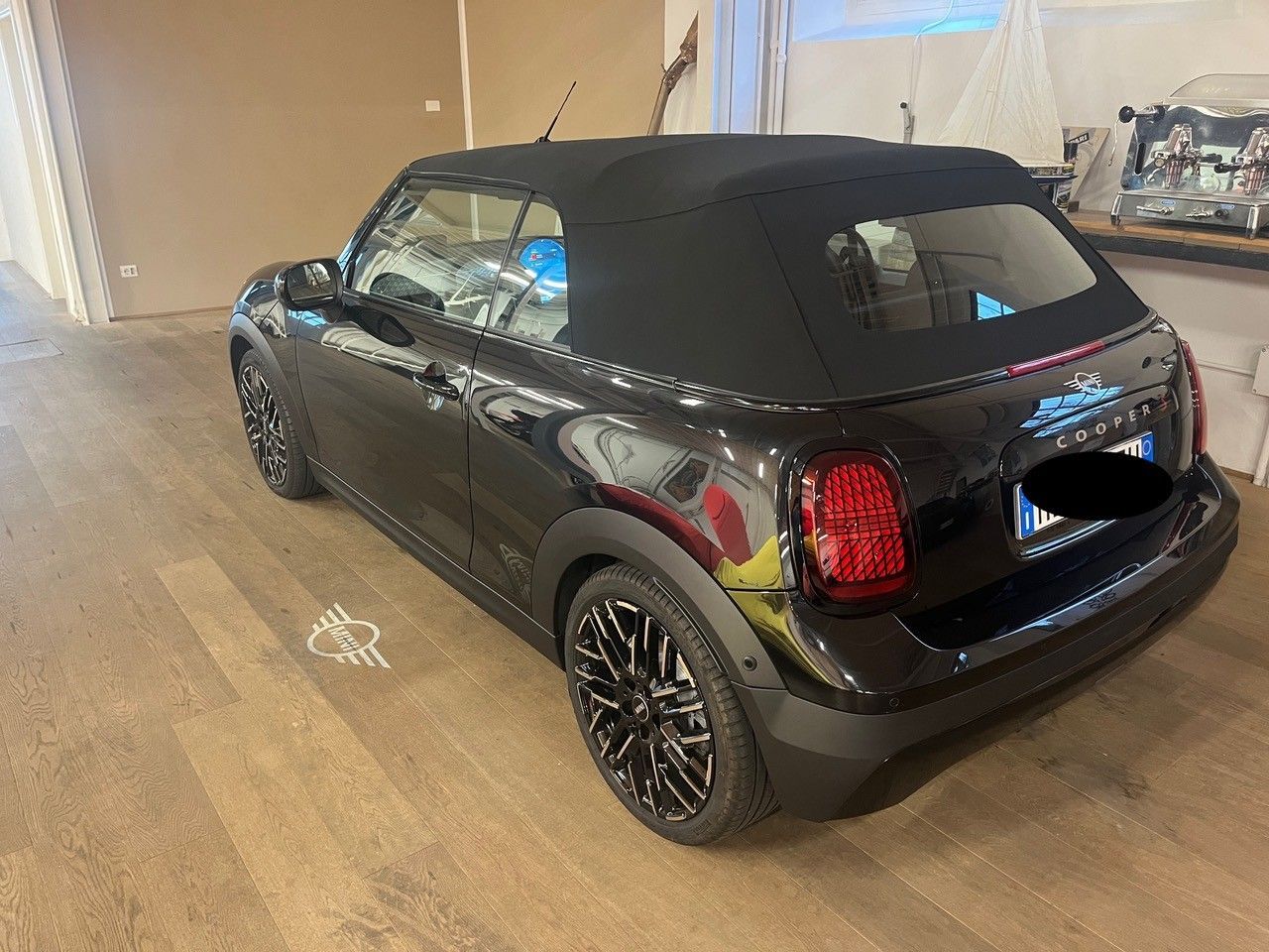 Mini Cooper decappottabile nera parcheggiata al chiuso su un pavimento lucidato.