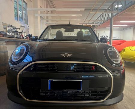 Auto sportiva nera in uno showroom, con auto coperte di rosso sullo sfondo.