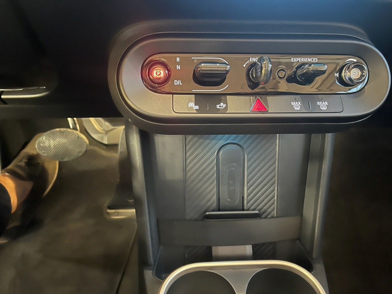 Pannello di controllo del climatizzatore interno dell'auto con pulsanti e manopole sopra la console centrale, con un piede visibile sulla sinistra.