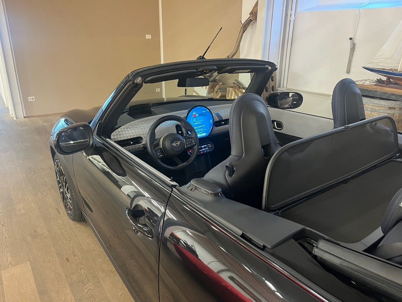 Auto sportiva decappottabile nera parcheggiata al chiuso, con cruscotto illuminato di blu e sedili in pelle nera.