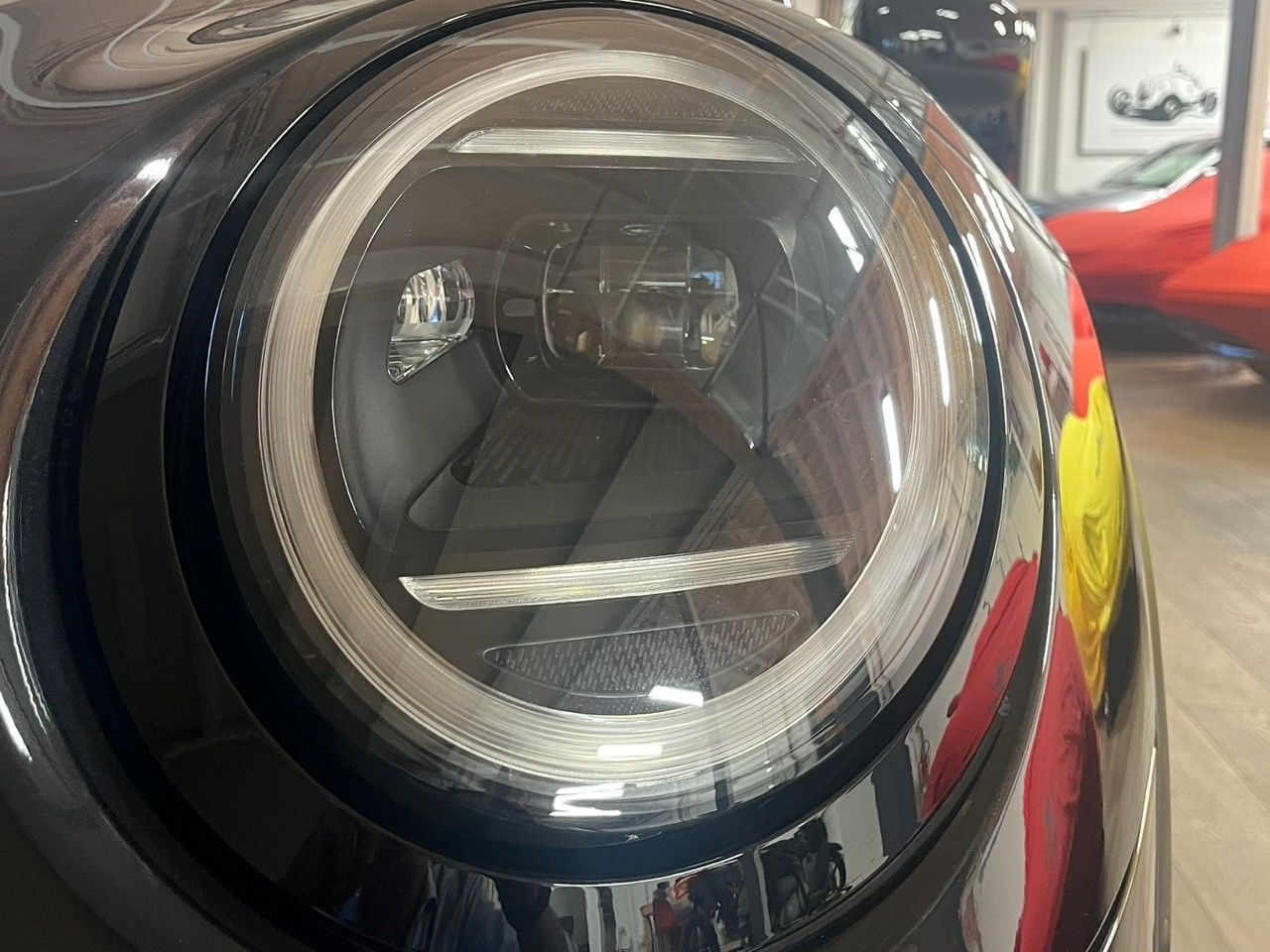 Primo piano del faro rotondo di un'auto nera con luce di posizione laterale gialla.