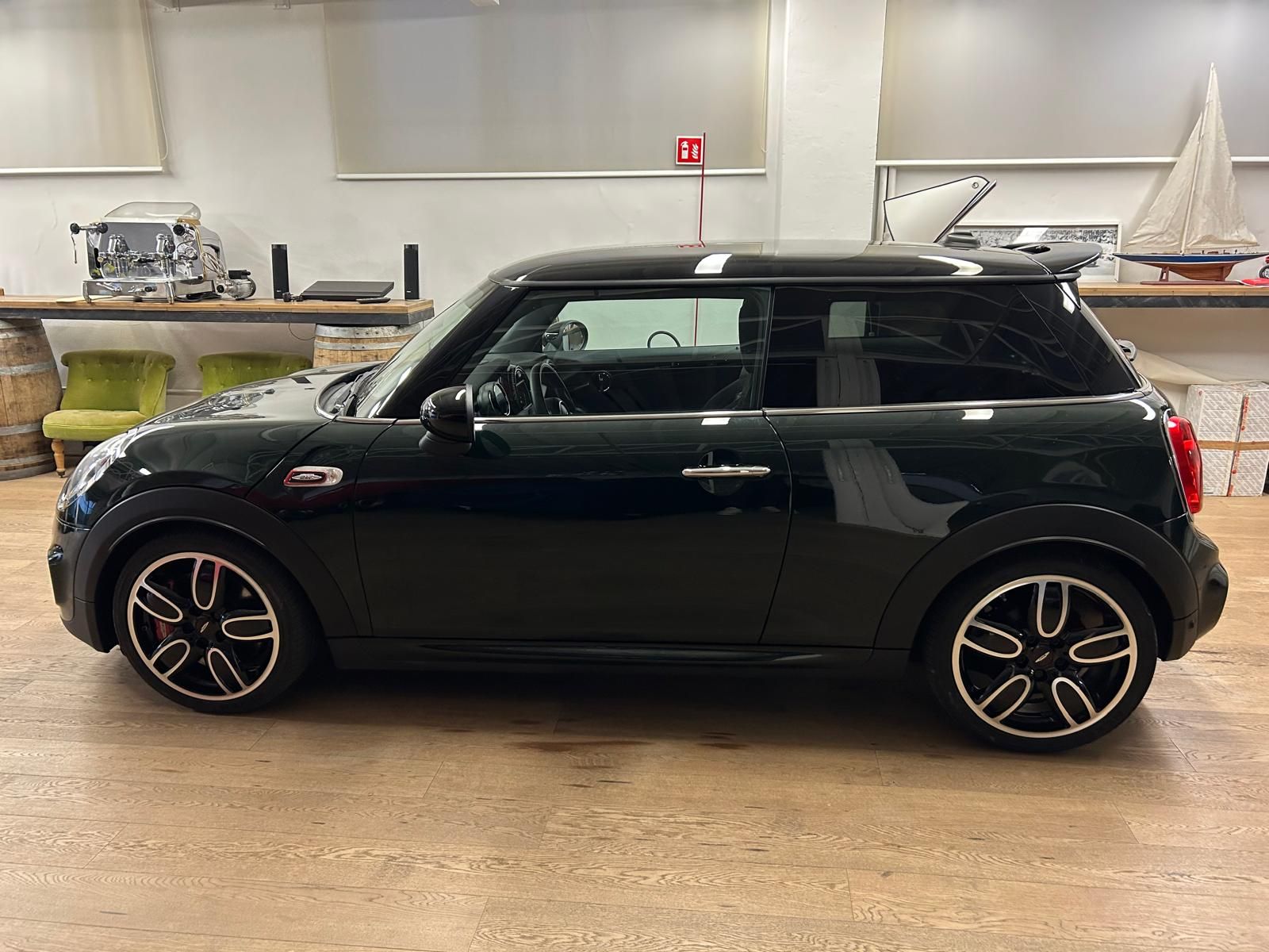 Una Mini Cooper nera parcheggiata all'interno su un pavimento di legno, vista di lato.