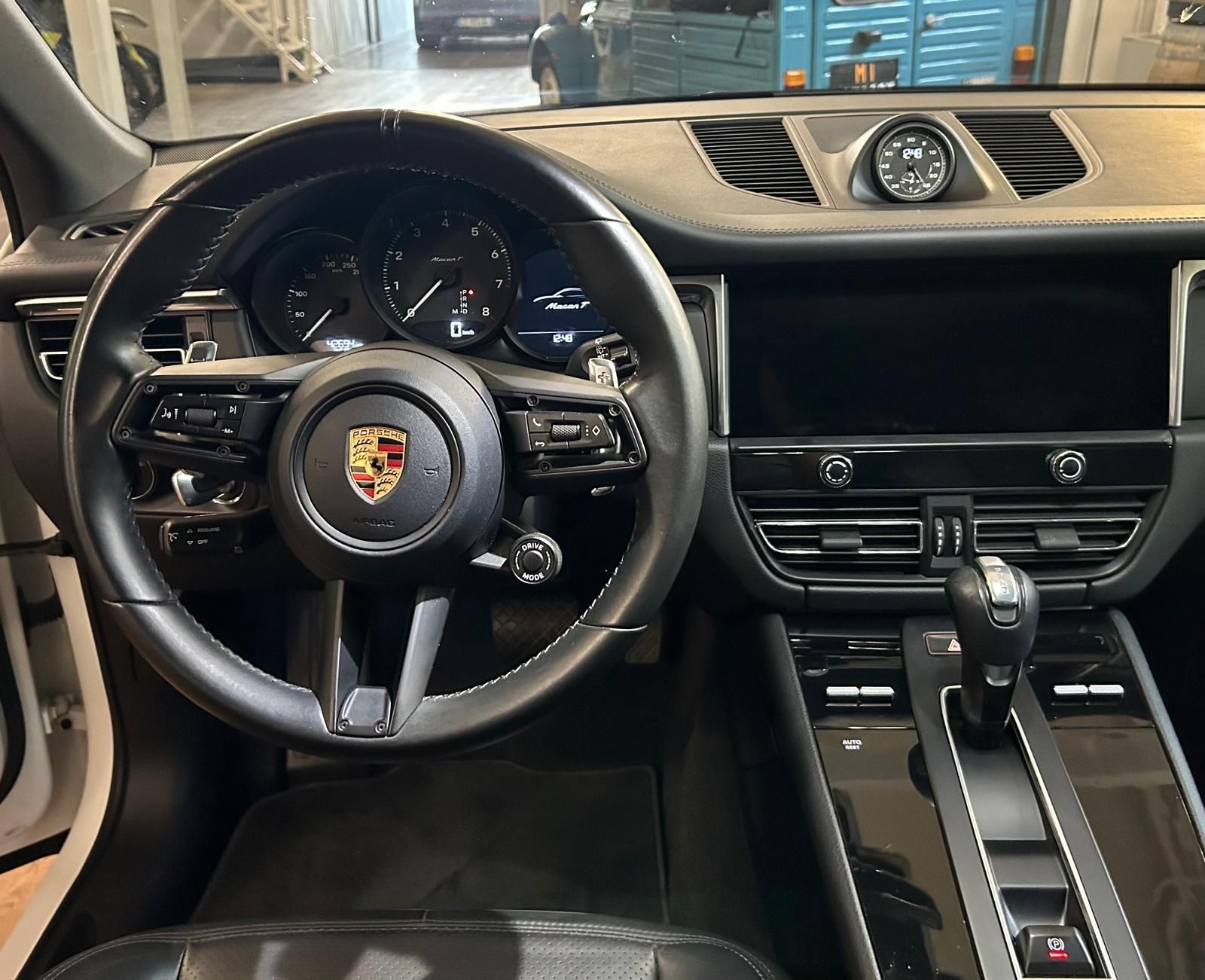 Vista degli interni di una moderna Porsche nera, con volante in pelle, indicatori sul cruscotto e console centrale.