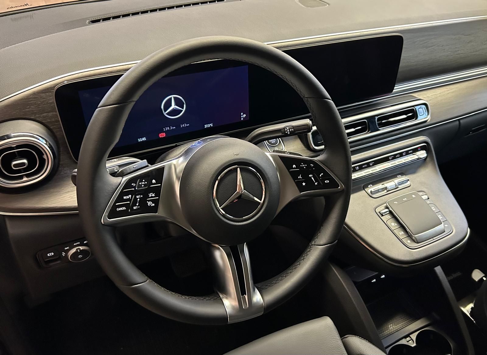 Vista interna di una moderna Mercedes-Benz nera, che mostra il volante, il cruscotto digitale e la console centrale.