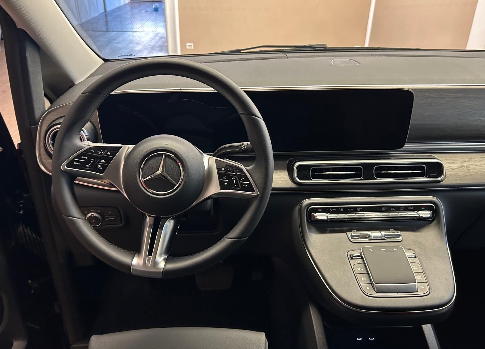 Gli interni di una moderna Mercedes-Benz nera, caratterizzati da volante in pelle, doppio display digitale e console centrale.