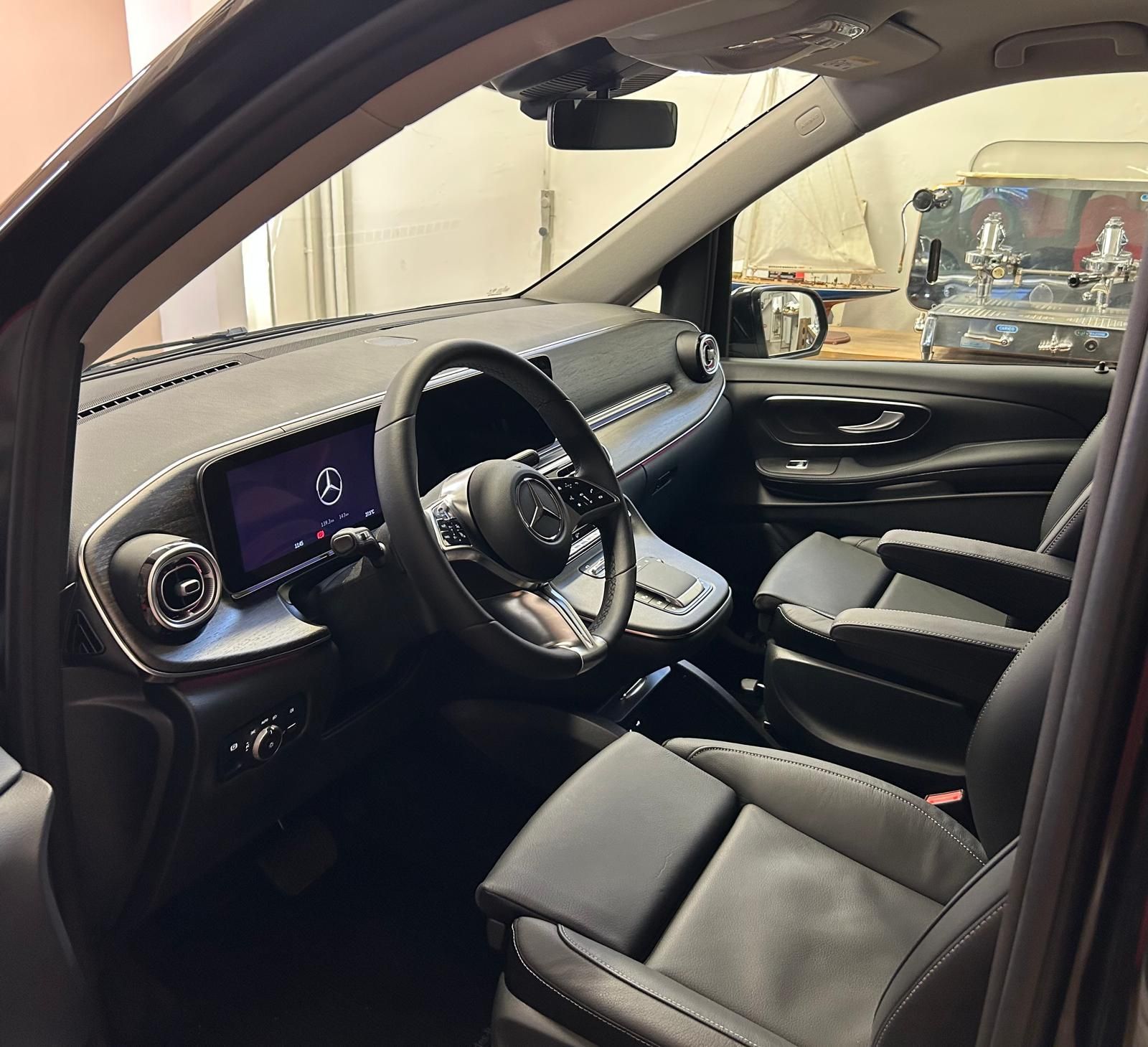 Vista interna di un furgone Mercedes-Benz nero con sedili in pelle, cruscotto digitale e volante moderno.