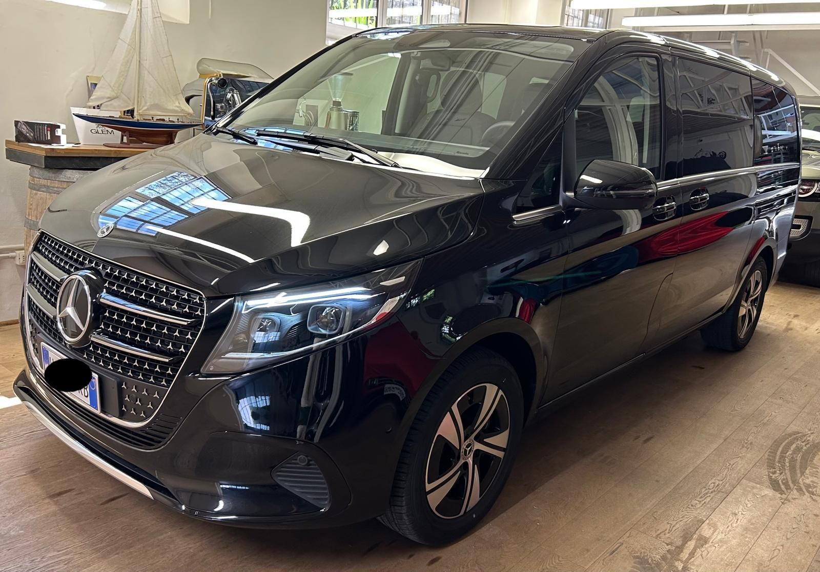 Un minivan Mercedes-Benz Classe V nero parcheggiato all'interno di un edificio, su un pavimento di colore chiaro, visto da un'angolazione di tre quarti anteriore.