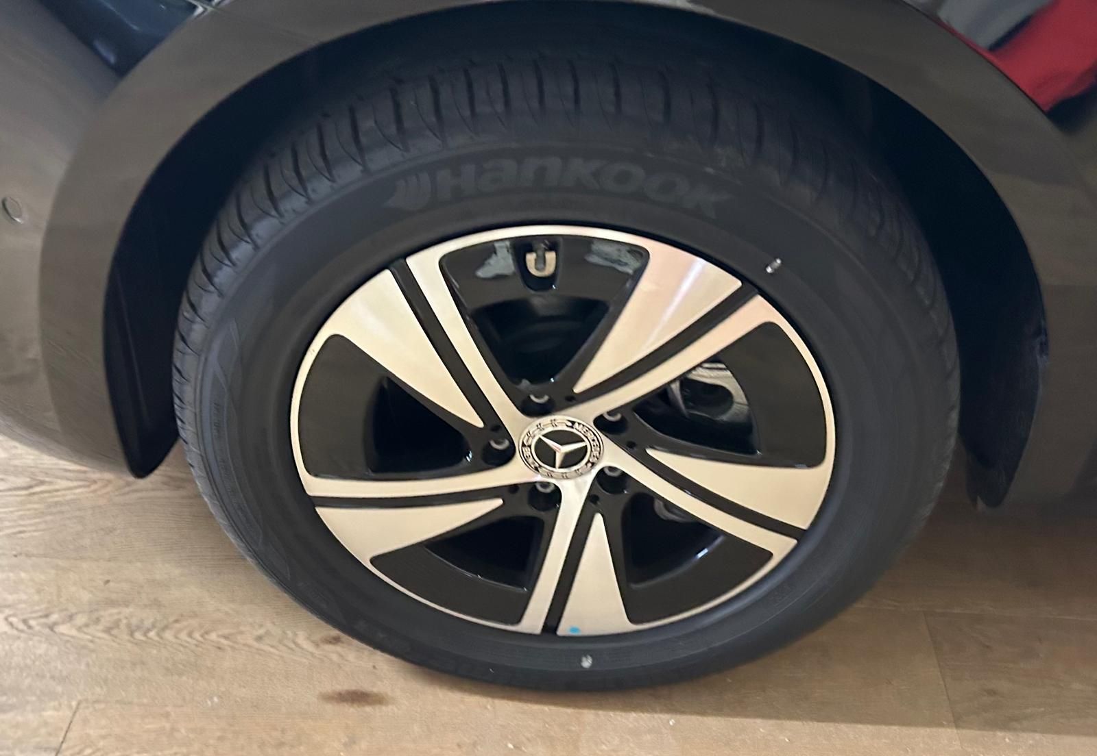 Primo piano di un cerchio in lega Mercedes-Benz con design a razze geometriche nere e argento, equipaggiato con uno pneumatico Hankook.