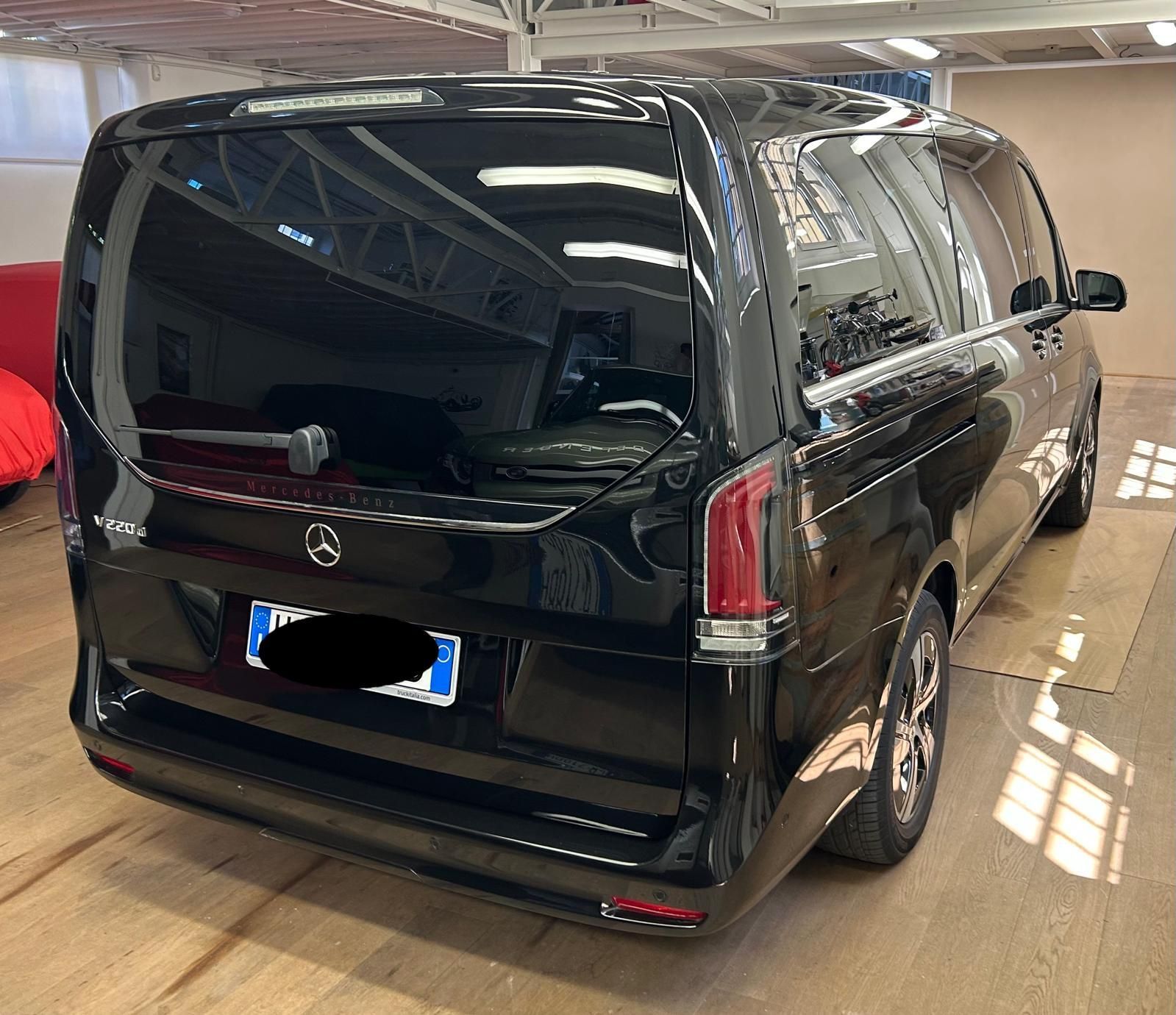 Un furgone Mercedes-Benz Classe V nero parcheggiato all'interno di uno spazio luminoso, simile a un magazzino, con pavimento in legno.