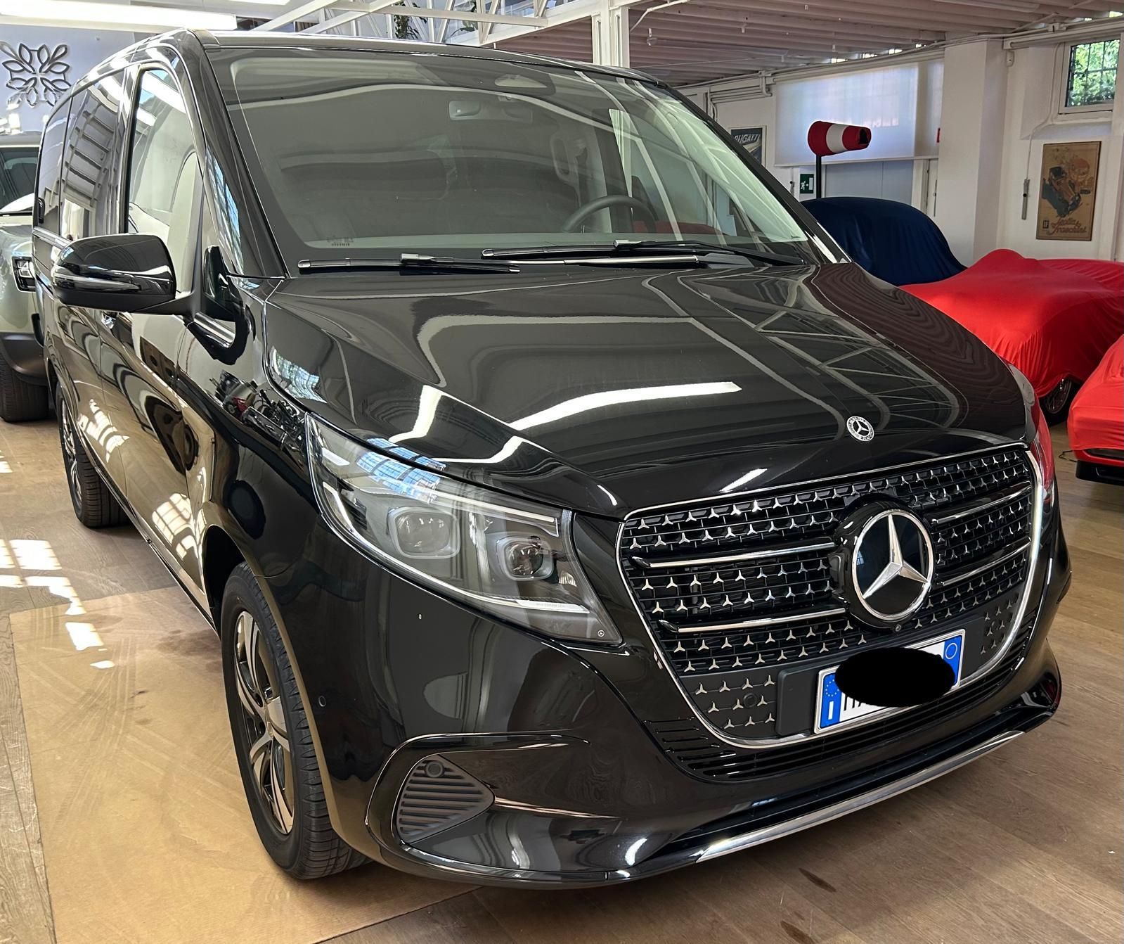 Un furgone Mercedes-Benz Classe V nero parcheggiato in uno showroom ben illuminato, con altri veicoli sullo sfondo.