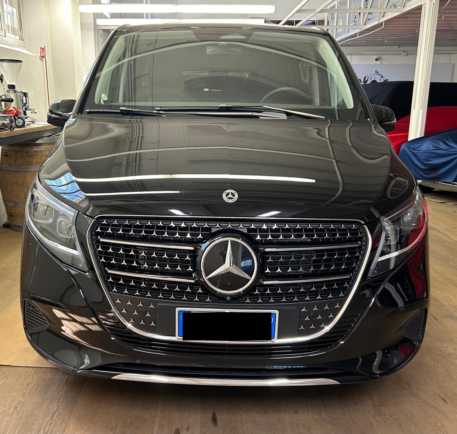 Un furgone Mercedes-Benz Classe V nero, con il frontale ben visibile e il logo in bella vista sulla griglia, è parcheggiato all'interno di un'officina.