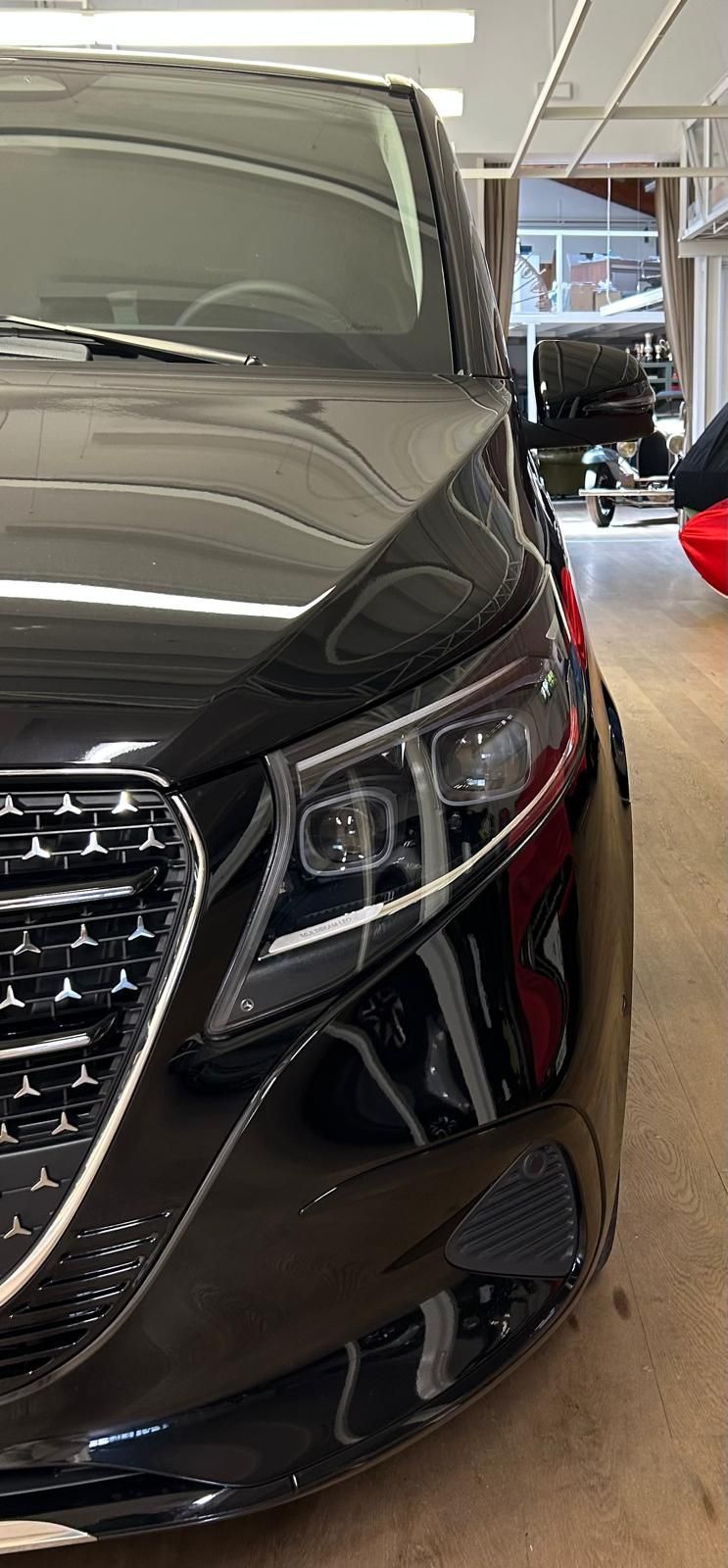 Una vista ravvicinata e angolata del faro anteriore, del cofano e della griglia cromata di un'auto di lusso nera in uno showroom.