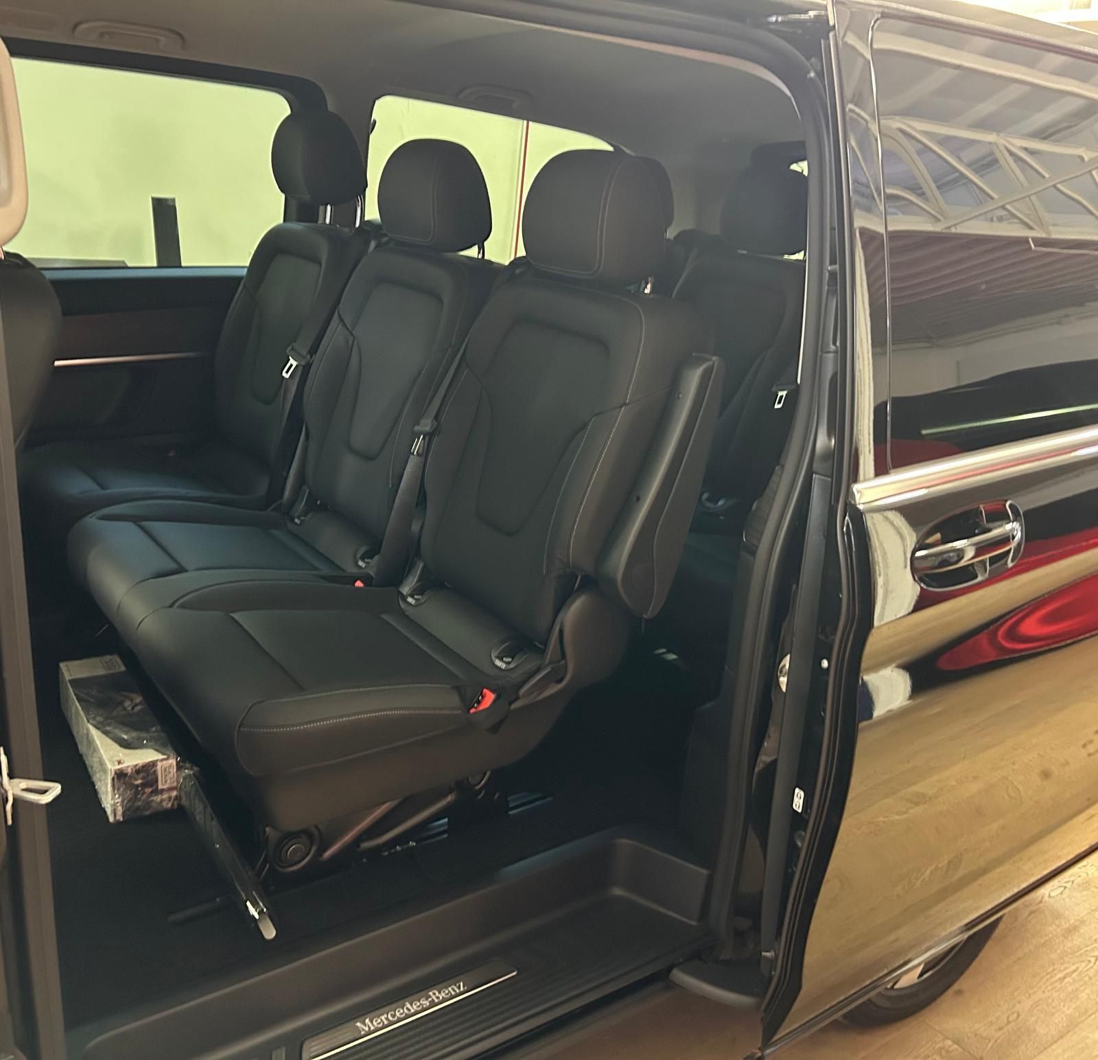 Vista laterale dell'interno di un furgone Mercedes-Benz nero con tre sedili in pelle nera rivolti in avanti.